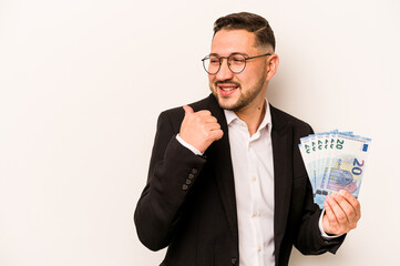 Business hispanic man holding banknotes isolated on white background points with thumb finger away, laughing and carefree.