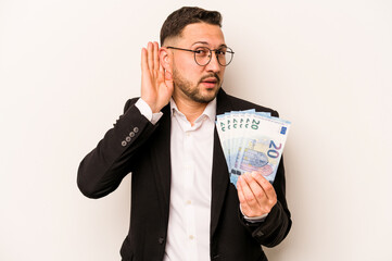 Business hispanic man holding banknotes isolated on white background trying to listening a gossip.