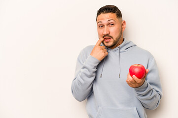 Hispanic man holding an apple isolated on white background relaxed thinking about something looking at a copy space.