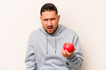 Hispanic man holding an apple isolated on white background screaming very angry and aggressive.