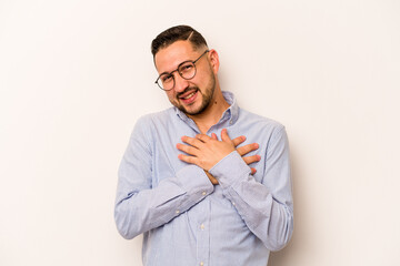 Young hispanic man isolated on white background laughing keeping hands on heart, concept of happiness.