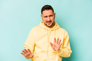 Young hispanic man isolated on blue background rejecting someone showing a gesture of disgust.