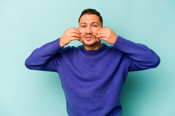 Young hispanic man isolated on blue background doubting between two options.