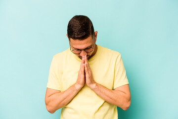 Young hispanic man isolated on blue background praying, showing devotion, religious person looking...