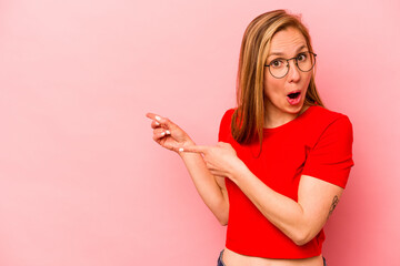 Young caucasian woman isolated on pink background pointing with forefingers to a copy space,...