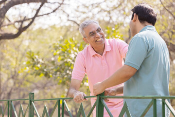 Happy senior man having friendly positive conversation with adult son at park