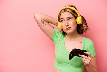 Young caucasian woman playing with a video game controller isolated on pink background touching back of head, thinking and making a choice. © Asier