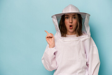 Young caucasian beekeeper woman isolated on blue background pointing to the side