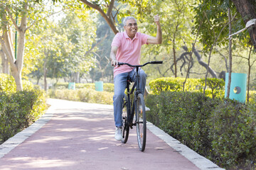 Cheerful senior man having fun riding bicycle at park