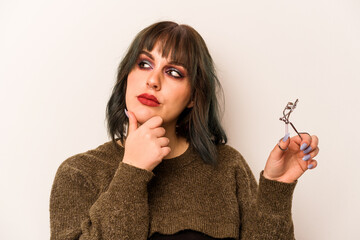 Young caucasian makeup artist woman holding a eyelash curler isolated on white background looking...