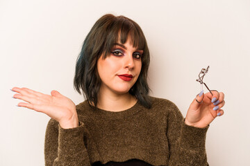 Young caucasian makeup artist woman holding a eyelash curler isolated on white background showing a...
