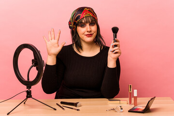 Young makeup artist woman doing a makeup tutorial isolated on pink background smiling cheerful...
