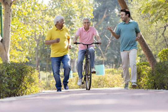 Senior man riding bicycle with other old man and son running while having fun at park
