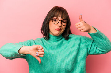 Young caucasian woman isolated on pink background showing thumbs up and thumbs down, difficult...