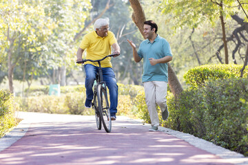 Cheerful senior man riding bicycle while son running at park