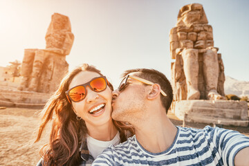 Happy traveler couple in love takes a selfie photo near the famous colossi of Memnon pharaoh...