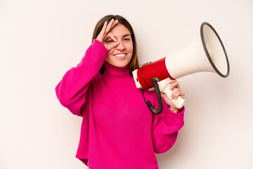 Young caucasian woman holding a megaphone isolated on white background excited keeping ok gesture on eye.