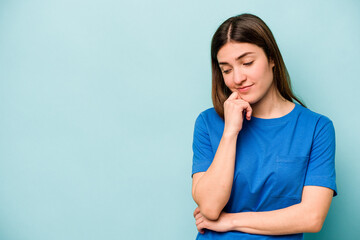 Young caucasian woman isolated on blue background looking sideways with doubtful and skeptical expression.