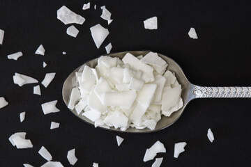 Close up of white soy wax flakes on spoon for candle making. Light texture of soy wax flakes. Ingredient for homemade candles. Ecological lifestyle