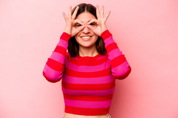 Young caucasian woman isolated on pink background showing okay sign over eyes