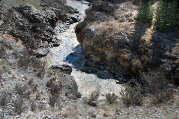 Muddy stream in mountain canyon. Yellow dirty river after flooding in early spring. Dry sheer cliffs form riverbed
