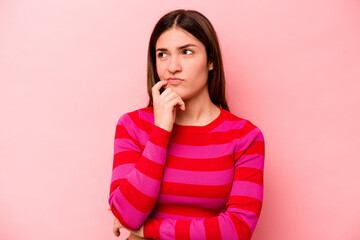 Young caucasian woman isolated on pink background thinking and looking up, being reflective, contemplating, having a fantasy.