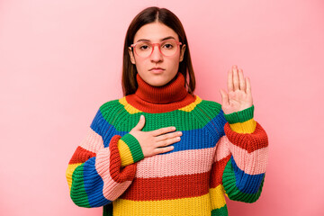 Young caucasian woman isolated on pink background taking an oath, putting hand on chest.