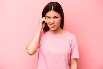 Young caucasian woman isolated on pink background covering ears with fingers, stressed and desperate by a loudly ambient.