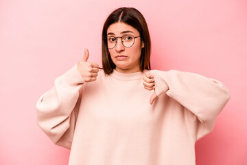 Young caucasian woman isolated on pink background showing thumbs up and thumbs down, difficult...