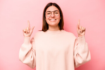Young caucasian woman isolated on pink background indicates with both fore fingers up showing a...