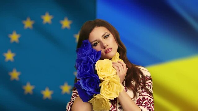 a woman in national clothes looks into the camera with love and anxiety because of the escalation of the military conflict in Ukraine, the Russian invasion against the background of the flag of Ukrain