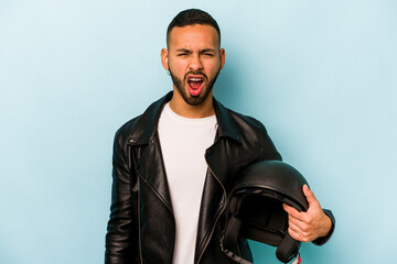 Young hispanic biker man isolated on blue background screaming very angry and aggressive.