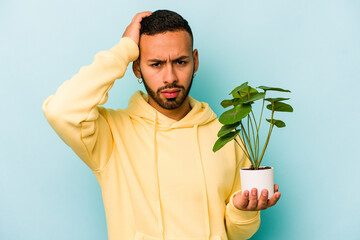 Young hispanic man holding a plant isolated on blue background being shocked, she has remembered...