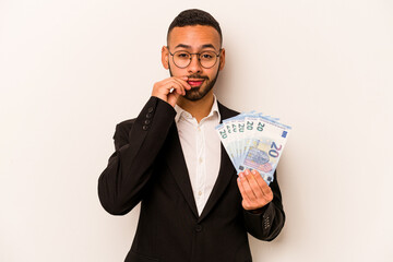 Young business hispanic man holding banknotes isolated on white background with fingers on lips keeping a secret.