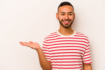 Fototapeta premium Young hispanic man isolated on white background showing a copy space on a palm and holding another hand on waist.