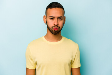 Young hispanic man isolated on blue background blows cheeks, has tired expression. Facial expression concept.