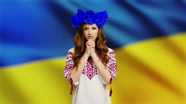 a woman in national clothes looks into the camera with love and anxiety because of the escalation of the military conflict in Ukraine, the Russian invasion against the background of the flag of Ukrain