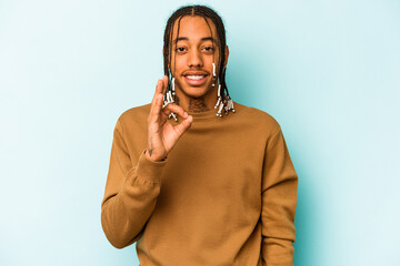 Young African American man isolated on blue background cheerful and confident showing ok gesture.