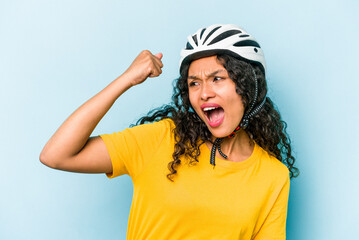 Young hispanic woman wearing a helmet bike isolated on blue background raising fist after a victory, winner concept.