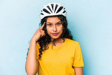 Young hispanic woman wearing a helmet bike isolated on blue background pointing temple with finger,...