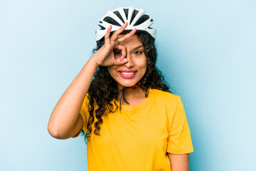 Young hispanic woman wearing a helmet bike isolated on blue background excited keeping ok gesture on eye.