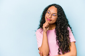 Young hispanic woman isolated on blue background relaxed thinking about something looking at a copy space.