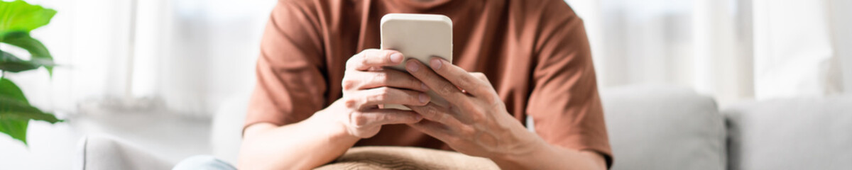 Technology Concept The man sitting next to a pot of plant, putting a small pillow on his lap, and checking something on his smartphone