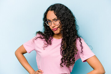 Young hispanic woman isolated on blue background frowning face in displeasure, keeps arms folded.