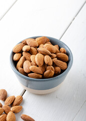 Raw brown almond seeds in ceramic bowl on the white wooden background.