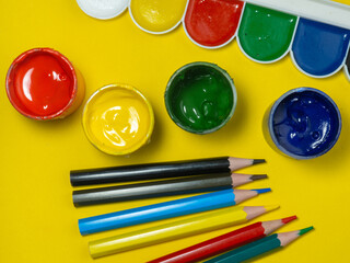 Jars of paint and pencils on a yellow background. Banks of gouache.   Creative background. Artist's...