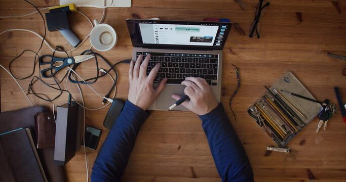 Top view on the wooden table where the programmer is working with a laptop and holding an electric cigarette. A home office with the mess that goes with it.