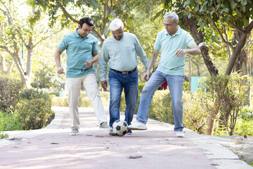 Two senior man with son having fun while playing football at park