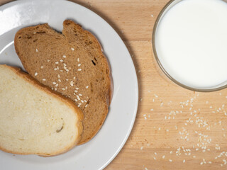 Pieces of rye and white bread with a glass of milk on a plate.  Bakery products with sesame seeds.