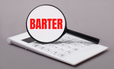 On a gray background, a white calculator and a magnifying glass with the text BARTER. Business...